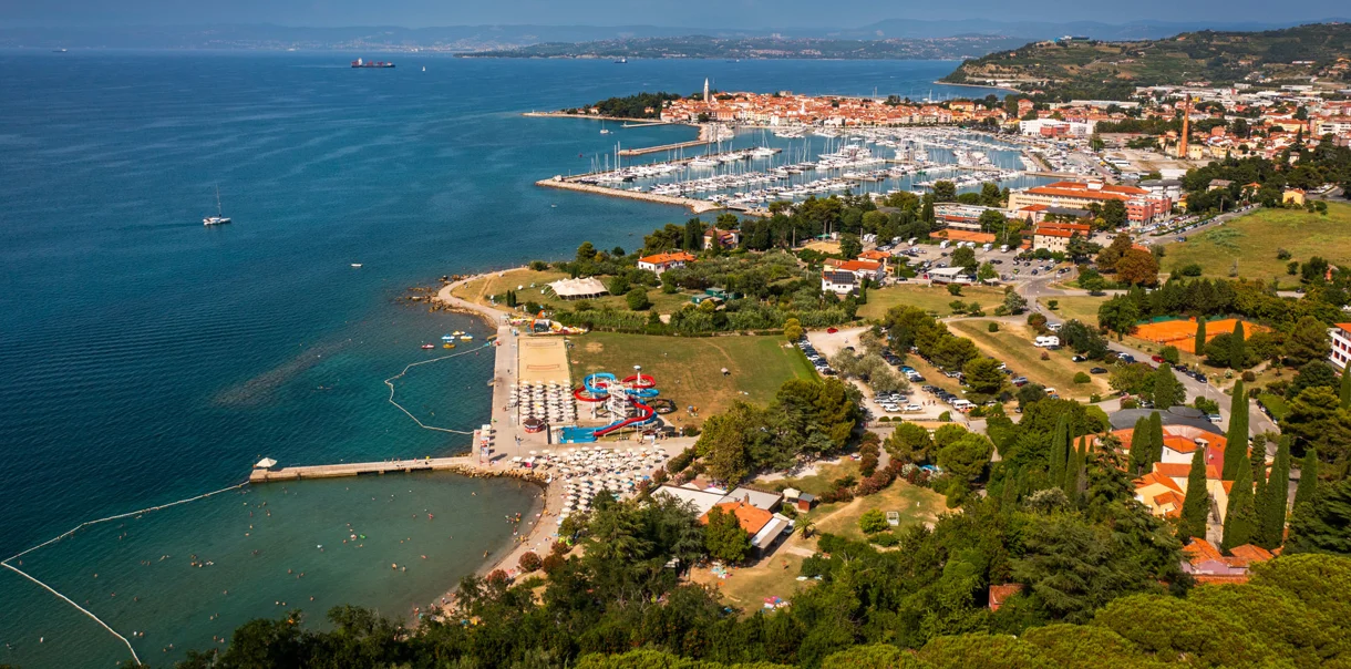 Panoramski pogled na slovensko obalo, ki vključuje pristanišče, hotelski kompleks, staro mestno jedro in zelene površine