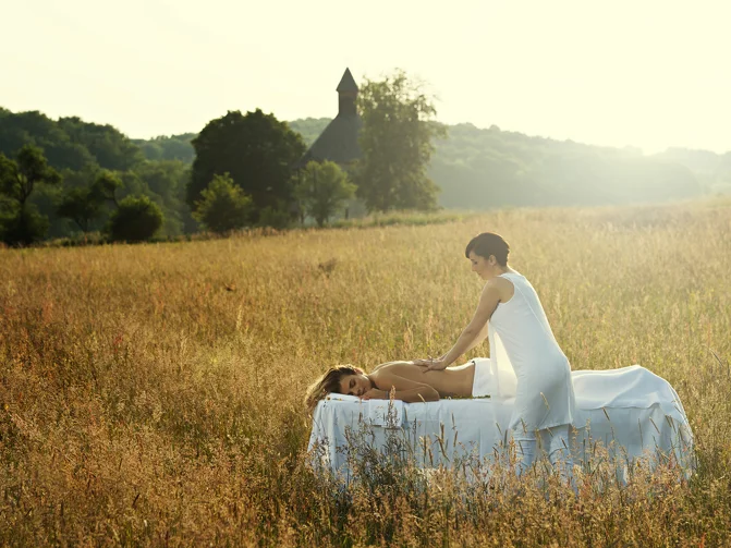 Ženska v beli obleki izvaja masažo hrbta na masažni mizi na rjavo-zelenem travniku