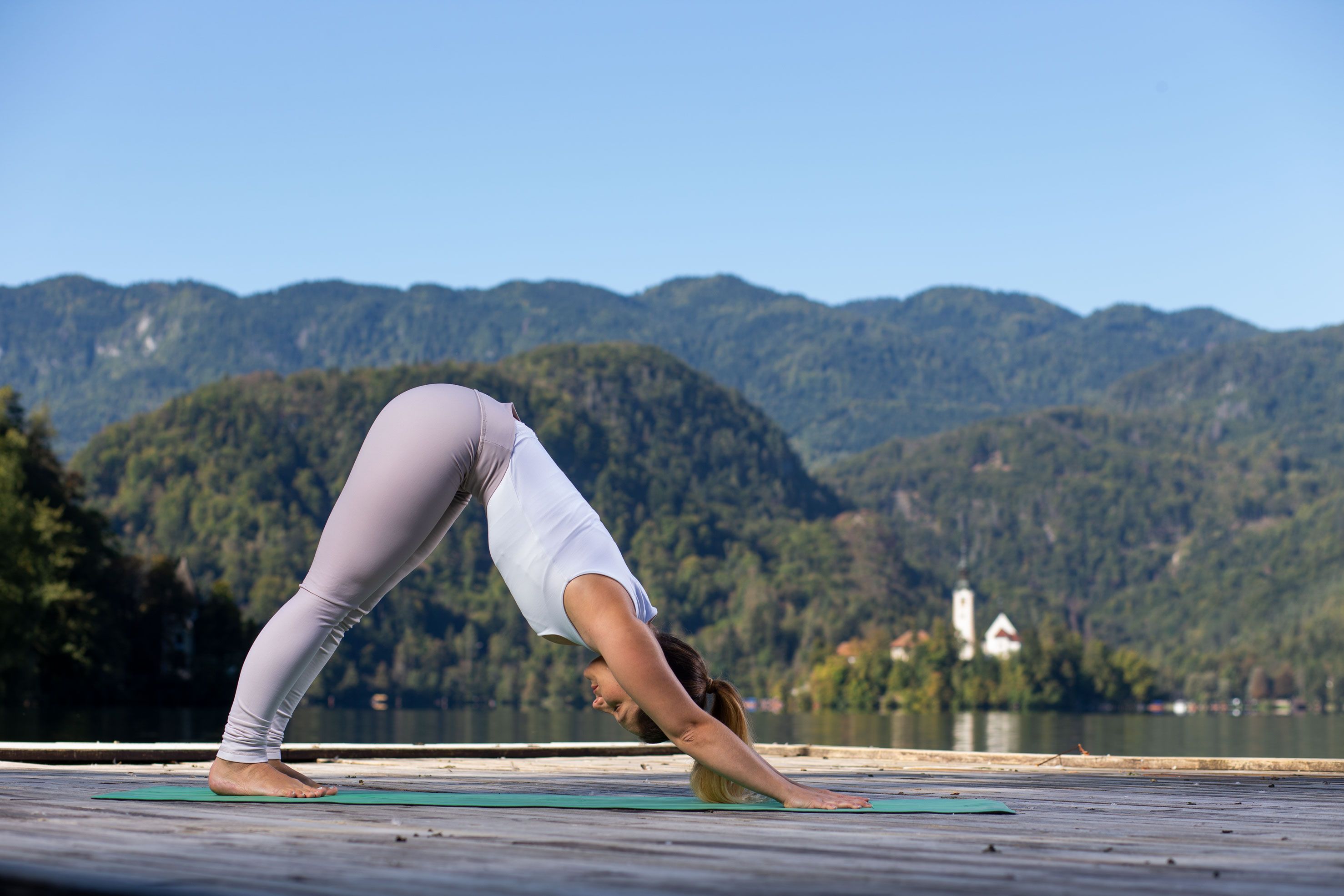 Ženska v položaju "strešica" izvaja jogo ob blejskem jezeru