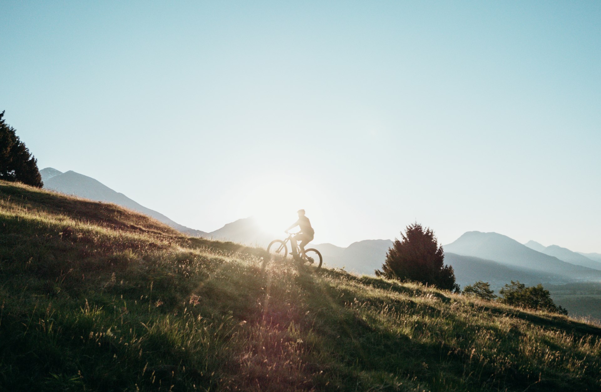 Radfahrer auf einem Bergweg bei Sonnenuntergang mit Blick auf die Berge.