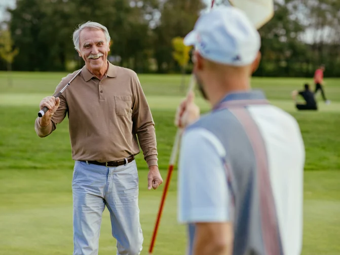 Moški v športnih oblačilih z golf palico v roki se pogovarja z drugim moškim na golf igrišču